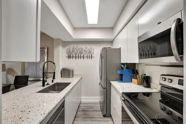 kitchen featuring white cabinetry, sink, light stone counters, appliances with stainless steel finishes, and light wood-type flooring