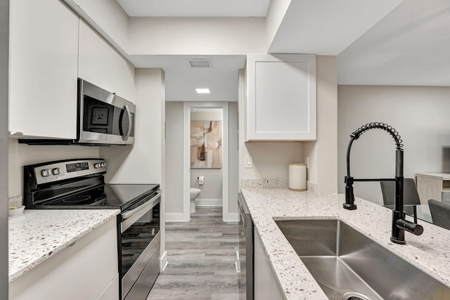 kitchen with stainless steel appliances, light stone counters, sink, white cabinetry, and light wood-type flooring