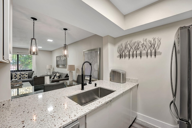 kitchen featuring light stone counters, stainless steel refrigerator, hanging light fixtures, sink, and hardwood / wood-style flooring