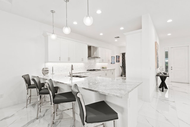 kitchen featuring wall chimney exhaust hood, sink, white cabinetry, hanging light fixtures, and kitchen peninsula