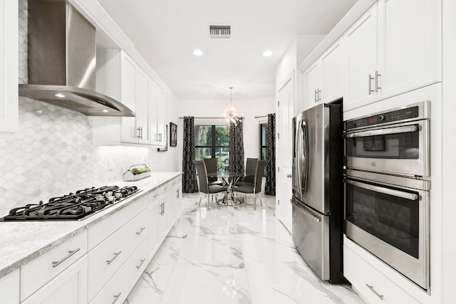 kitchen featuring wall chimney range hood, appliances with stainless steel finishes, white cabinetry, backsplash, and light stone countertops