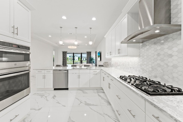 kitchen with pendant lighting, white cabinetry, wall chimney exhaust hood, and appliances with stainless steel finishes