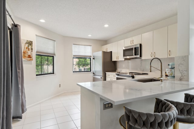 kitchen with sink, stainless steel appliances, a kitchen breakfast bar, light stone counters, and kitchen peninsula