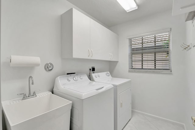 clothes washing area with cabinets, washing machine and dryer, light tile patterned floors, and sink