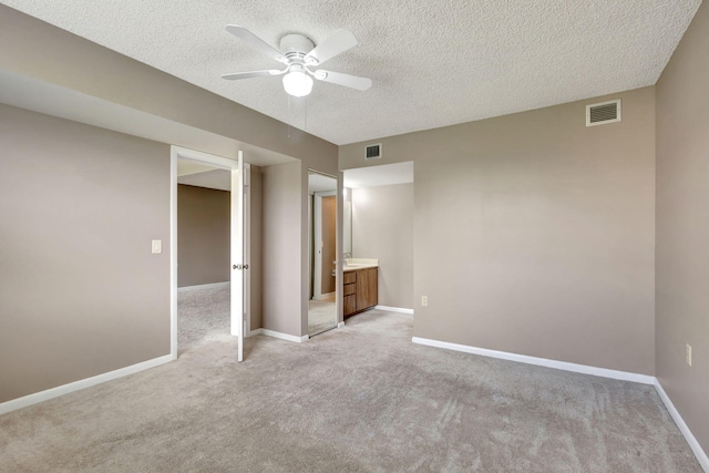 unfurnished bedroom with a textured ceiling, light carpet, ceiling fan, and connected bathroom