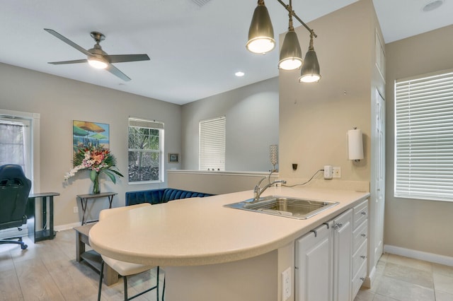 kitchen with decorative light fixtures, sink, light hardwood / wood-style floors, white cabinets, and kitchen peninsula