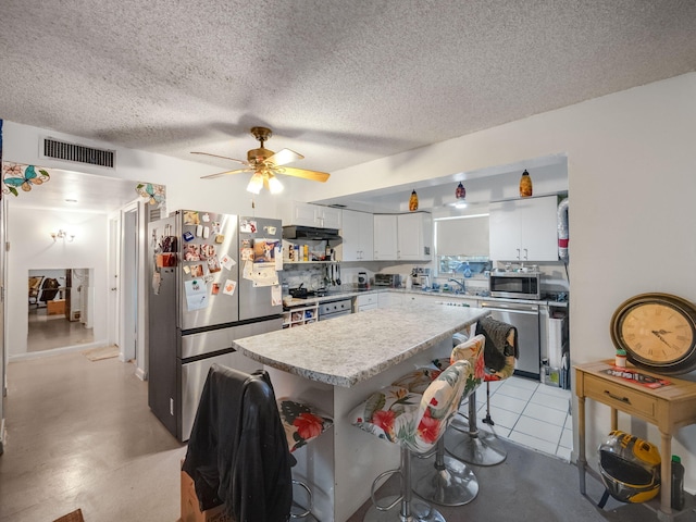 kitchen featuring stainless steel appliances, a textured ceiling, a kitchen bar, white cabinets, and ceiling fan