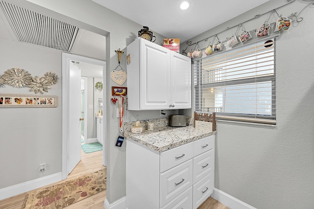 kitchen with white cabinetry, light wood-type flooring, and light stone countertops