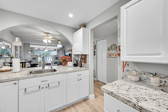 kitchen with white cabinets, sink, ceiling fan, light wood-type flooring, and decorative light fixtures