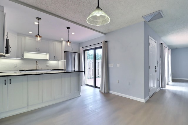 kitchen featuring decorative backsplash, sink, wood-type flooring, white cabinetry, and hanging light fixtures