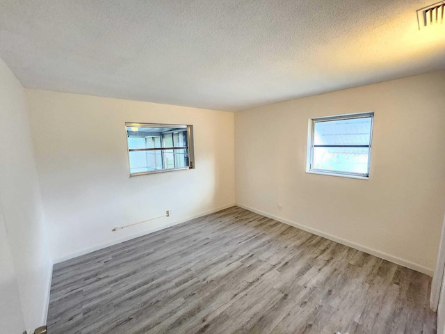 spare room with a textured ceiling and light hardwood / wood-style floors