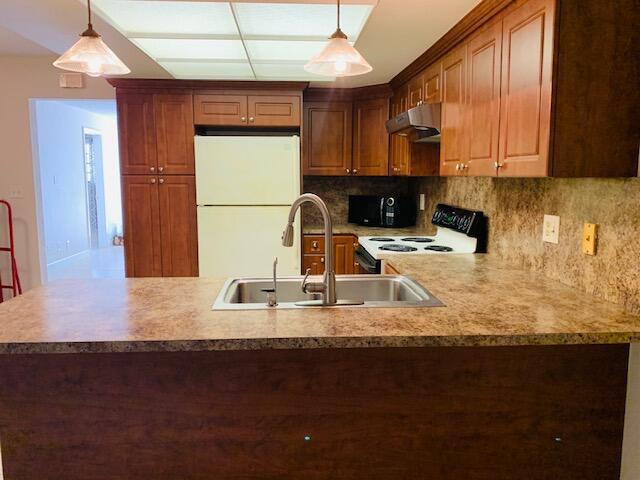 2727-29 NE 30th Ave, Lighthouse Point, FL 33064 - kitchen with freestanding refrigerator, under cabinet range hood, stove, tasteful backsplash, and decorative light fixtures