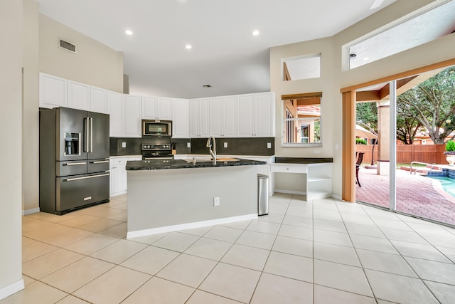 kitchen with stove, a kitchen island with sink, dark stone counters, a high ceiling, and high end refrigerator