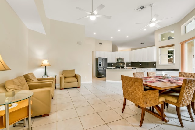 tiled dining space with ceiling fan and a high ceiling