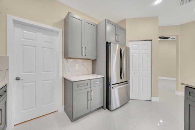 kitchen with light tile patterned floors, stainless steel fridge, gray cabinetry, and tasteful backsplash