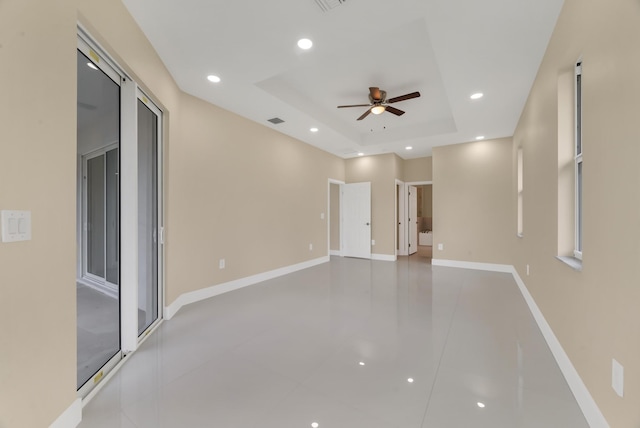 empty room with ceiling fan and a tray ceiling