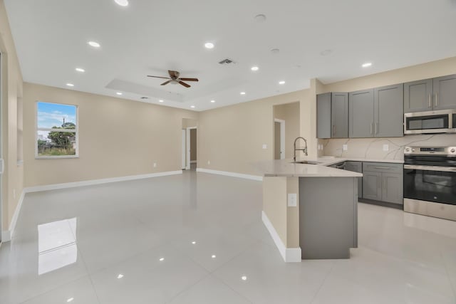 kitchen featuring stainless steel appliances, sink, kitchen peninsula, a tray ceiling, and gray cabinetry