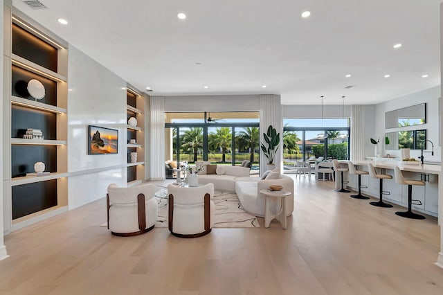 living room featuring built in shelves, a wealth of natural light, light hardwood / wood-style flooring, and sink