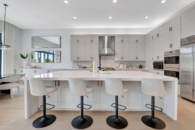 kitchen featuring built in appliances, wall chimney exhaust hood, a kitchen bar, and a large island