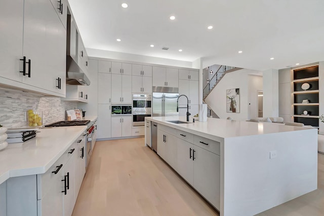 kitchen with a spacious island, sink, light wood-type flooring, premium appliances, and white cabinetry