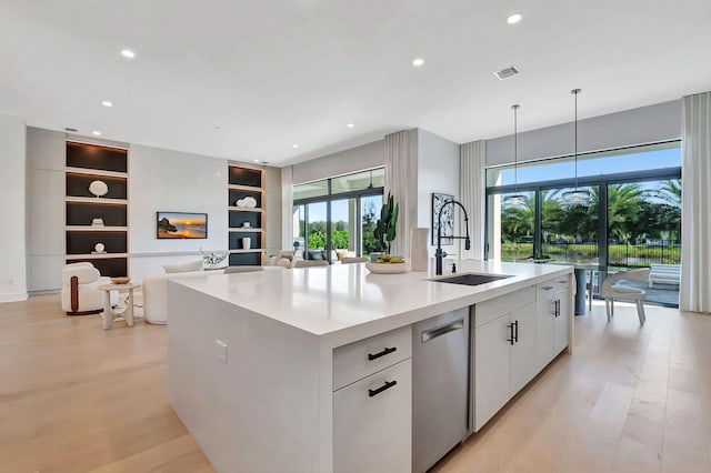 kitchen with white cabinets, light hardwood / wood-style flooring, a kitchen island with sink, and sink