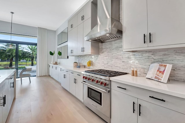 kitchen with wall chimney exhaust hood, hanging light fixtures, light hardwood / wood-style flooring, luxury stove, and decorative backsplash