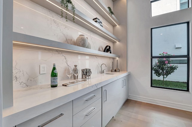 bar featuring decorative backsplash, light stone counters, sink, light hardwood / wood-style flooring, and white cabinetry