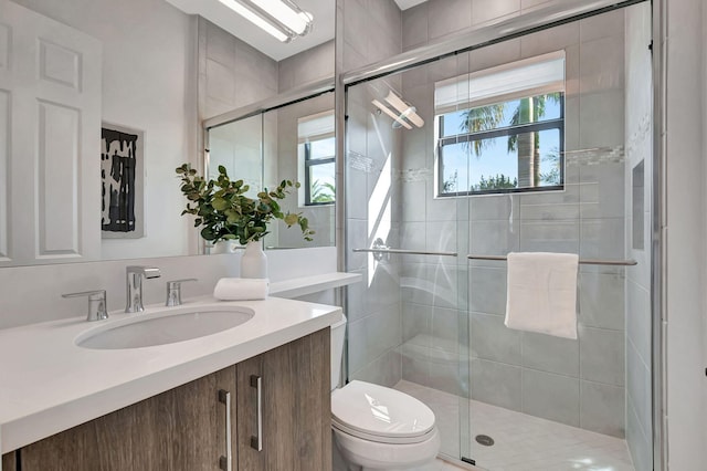 bathroom featuring vanity, toilet, a shower with shower door, and a wealth of natural light