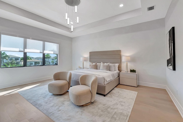 bedroom featuring a raised ceiling and light wood-type flooring