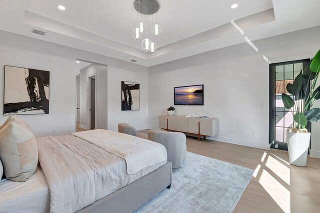 bedroom featuring a chandelier, a tray ceiling, and light hardwood / wood-style flooring