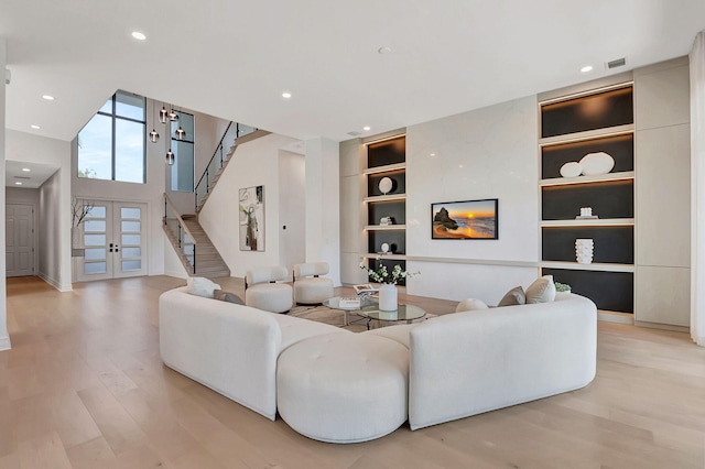 living room with light hardwood / wood-style floors, built in features, a high ceiling, and french doors