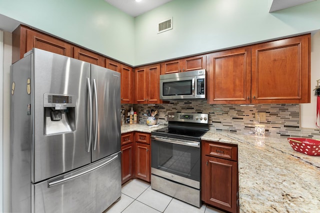 kitchen featuring light tile patterned floors, a towering ceiling, tasteful backsplash, light stone counters, and stainless steel appliances