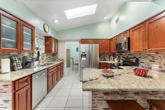 kitchen featuring light stone countertops, sink, stainless steel appliances, lofted ceiling with skylight, and a breakfast bar area