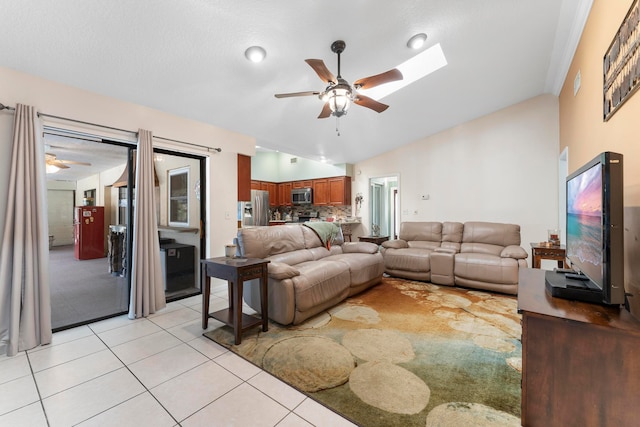 living room with light tile patterned flooring, ceiling fan, and vaulted ceiling with skylight