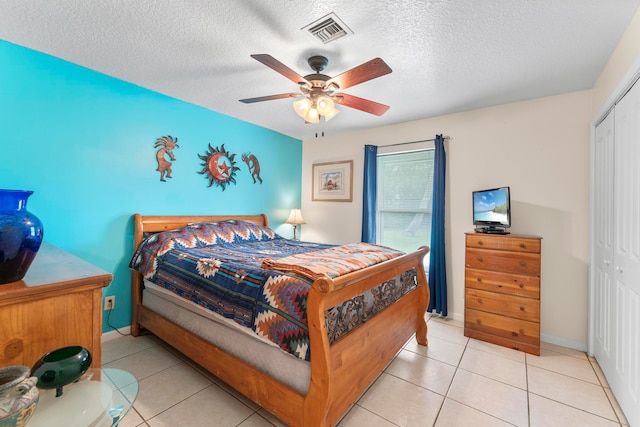 bedroom featuring ceiling fan, a closet, light tile patterned flooring, and a textured ceiling