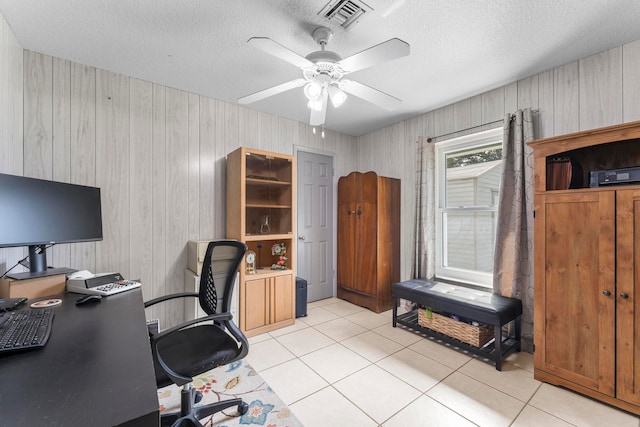 tiled home office featuring wooden walls, ceiling fan, and a textured ceiling