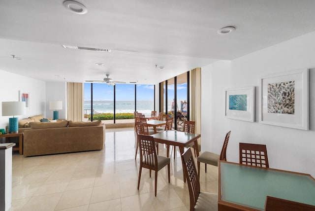 dining space featuring ceiling fan, a water view, light tile patterned floors, and a wall of windows