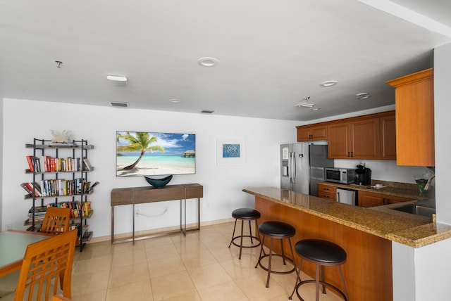 kitchen featuring a breakfast bar, stone counters, light tile patterned floors, kitchen peninsula, and stainless steel appliances