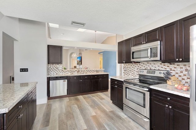 kitchen with dark brown cabinetry, decorative backsplash, stainless steel appliances, and light hardwood / wood-style floors