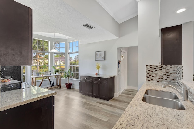 kitchen featuring backsplash, sink, light wood-type flooring, a textured ceiling, and decorative light fixtures