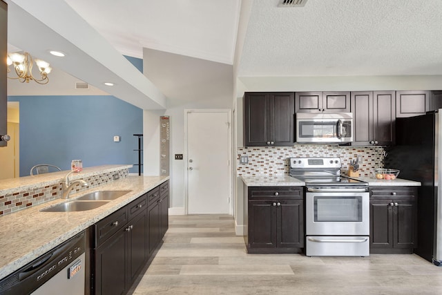 kitchen with appliances with stainless steel finishes, light wood-type flooring, tasteful backsplash, sink, and lofted ceiling