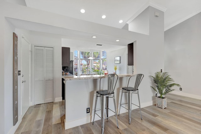 kitchen with dark brown cabinetry, light stone countertops, kitchen peninsula, a breakfast bar area, and light wood-type flooring