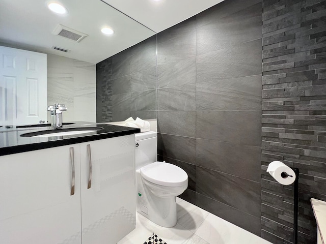 bathroom with toilet, vanity, tile walls, and tile patterned flooring