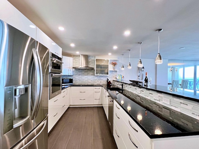 kitchen featuring white cabinetry, appliances with stainless steel finishes, decorative light fixtures, kitchen peninsula, and wall chimney exhaust hood