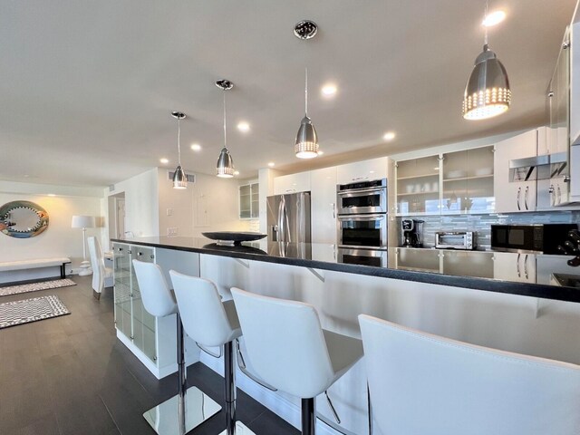 kitchen featuring dark hardwood / wood-style flooring, hanging light fixtures, backsplash, white cabinetry, and appliances with stainless steel finishes