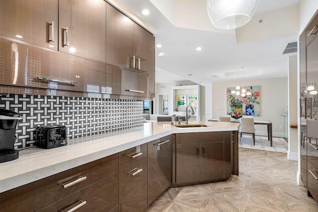 kitchen featuring sink, decorative backsplash, dark brown cabinetry, light stone counters, and light parquet flooring