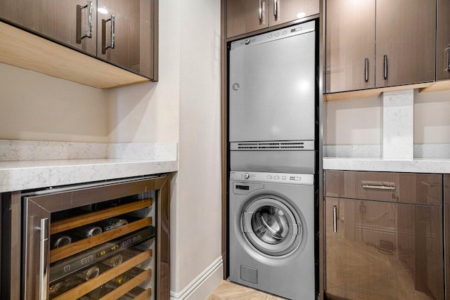 laundry area with beverage cooler, stacked washing maching and dryer, indoor bar, and light wood-type flooring