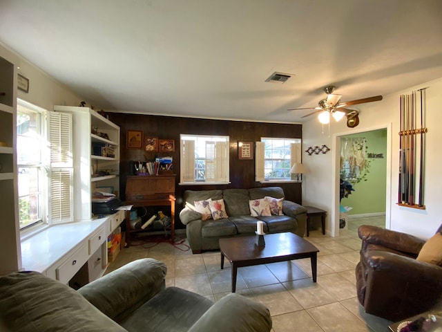 tiled living room featuring wood walls, crown molding, and ceiling fan