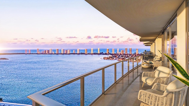 balcony at dusk featuring a water view