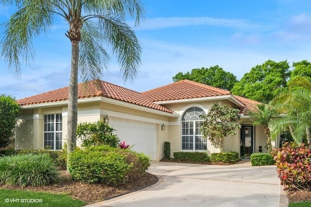 mediterranean / spanish home with a tiled roof, stucco siding, an attached garage, and driveway